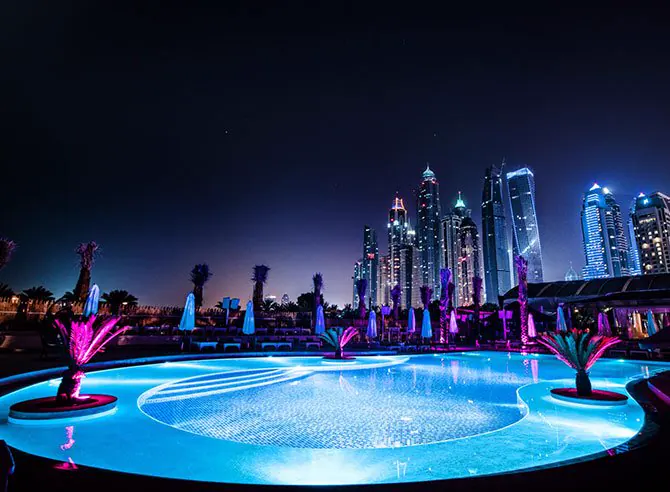 The pool lit at night, with the Dubai Marina skyline